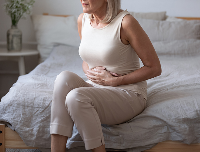 woman sitting on bed holding her stomach in pain